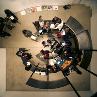 A bird's-eye view of a configuration of pieces of curved furniture, which resembles a multi-teared semi-circular amphitheatre. Visitors sit on it.