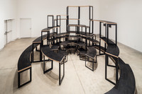 An image facing into the gallery from the doorway. Adrian Blackwell's Furnishing Positions is centered in the space, in a configuration resembling a multi-teared semi-circular amphitheatre, with various heights of furniture—some much higher than a person could safely reach to sit or stand on.