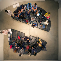 A bird's eye view of the Adrian Blackwell's Furnishing Positions sculpture, configured to resemble two semi-circular amphitheatres facing each other. Many people sit on the sculpture.