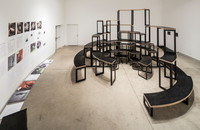 A view facing into the gallery, with Adrian Blackwell's furniture centered in the space, and a collection of broadsheets along the left wall.