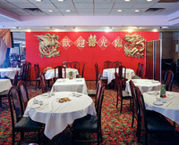 Interior view of a Chinese restaurant with tables for four to six people in the foreground and a wall ornated with Chinese symbols in the background.