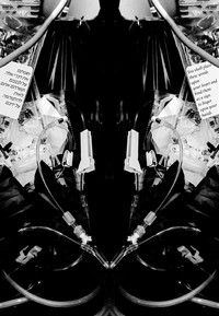 A close - up black - and - white photograph of discarded intravenous  is mirrored vertically from the center, creating a symmetrical image in which the machine is abstracted. White labels appear on solution bags mirrored on the right and left sides. The label on the left is in Hebrew, and the label on the right is in English and reads 