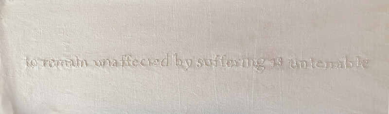 Off - white hand - embroidered text is centered on an off - white linen sheet, reading 